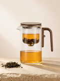 The Magnetic Release Teapot in glass and walnut wood, filled with amber tea